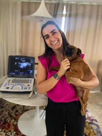 Integrante da equipe RAD com um cão no colo, ao lado de um aparelho de ultrassom portátil